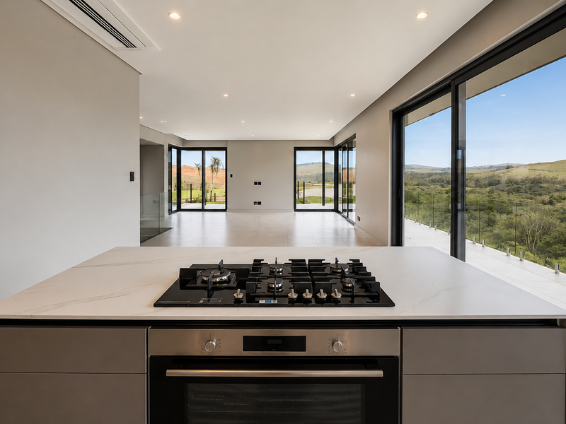 Modern open-plan kitchen area featuring a central island with built-in gas cooktop and oven, flowing into a spacious living area with expansive scenic views.