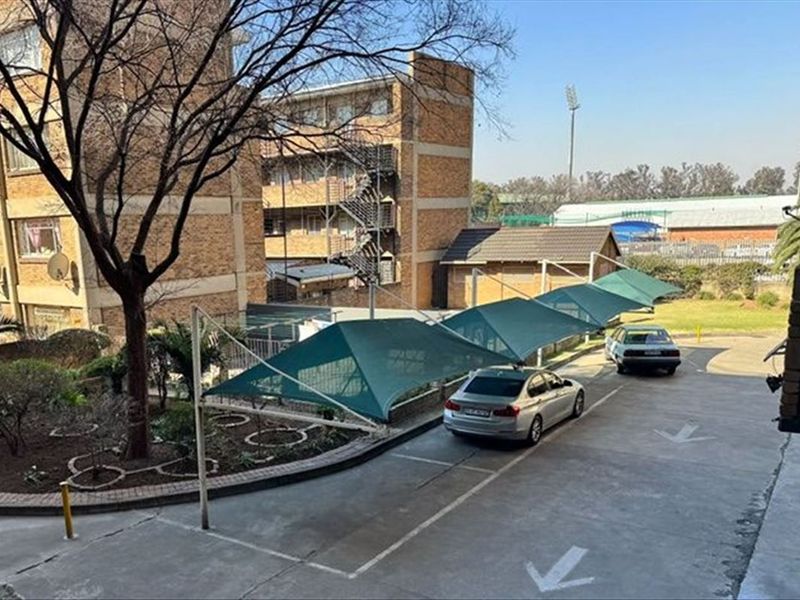 View of the apartment complex exterior featuring paved parking bays with shade cloth carports and established garden areas.