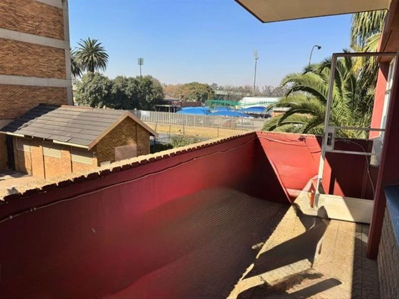 An open-air balcony featuring tiled flooring and a metal balustrade, offering an elevated view of the surrounding neighborhood.