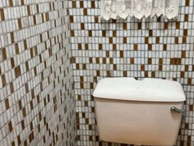 A compact bathroom featuring dated mosaic wall tiling and a standard toilet suite.