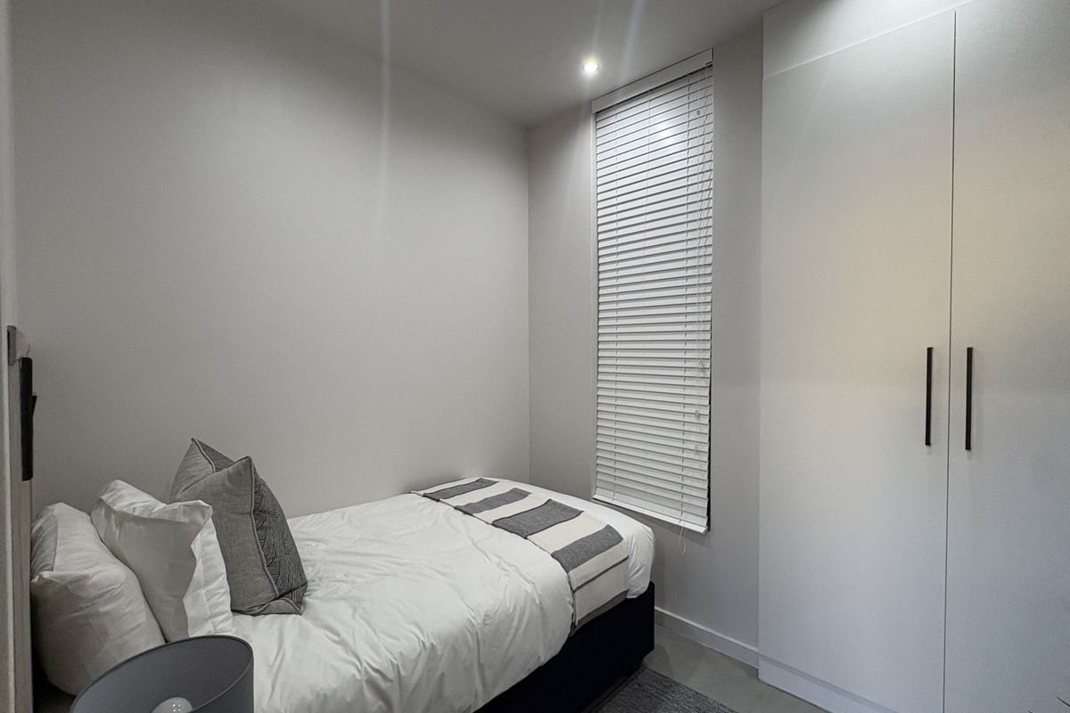 A compact, modern bedroom featuring a built-in wardrobe, venetian blinds, and recessed ceiling lighting, presented in a clean and well-maintained condition.