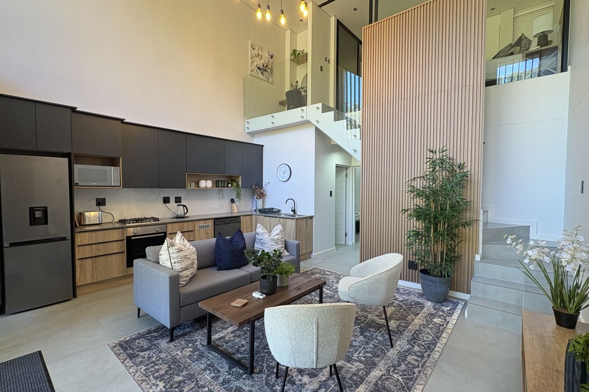 Modern open-plan living area featuring a sleek kitchen with built-in appliances, timber slat feature wall, and a staircase with glass balustrade.