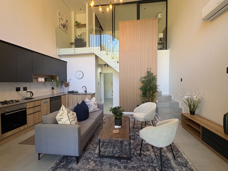 Modern open-plan living area featuring a sleek kitchen with integrated appliances, a mezzanine level with glass balustrades, and a striking slatted wood feature wall.