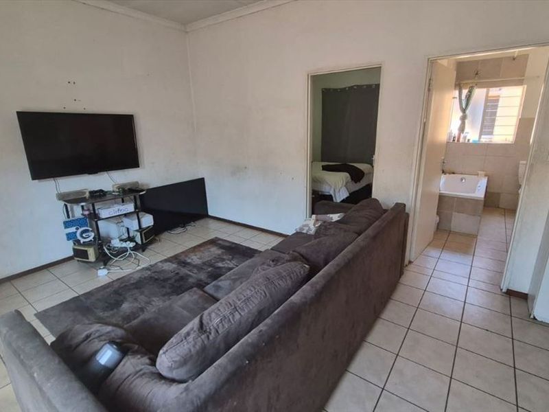 A living room area featuring tiled flooring and access to adjacent bedroom and bathroom spaces, showing signs of wear on walls and finishes.