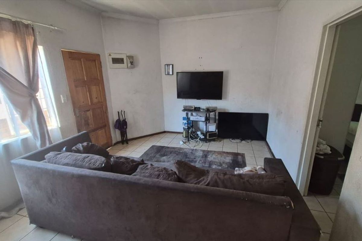 A living room featuring tiled flooring and a timber entrance door, currently showing signs of wear on the walls and finishes.