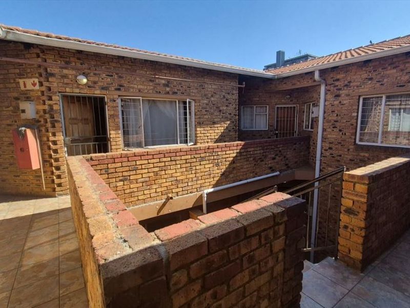 An exterior view of an apartment complex featuring face brick walls, tiled walkways, and secure access points with metal security gates.