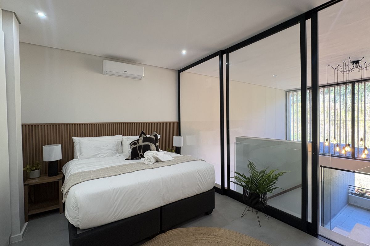 Modern bedroom featuring a slatted timber headboard, split-system air conditioning, and a sleek black-framed glass partition overlooking the lower level.