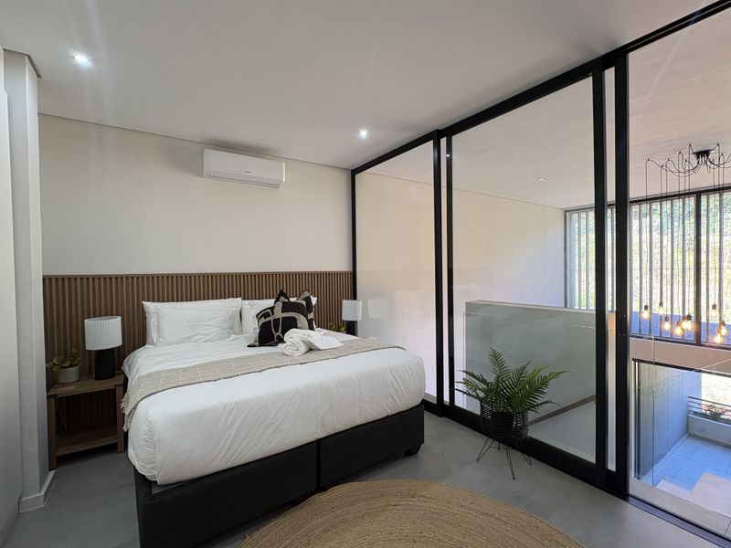 Modern bedroom featuring a slatted timber headboard, split-system air conditioning, and a sleek black-framed glass partition overlooking the lower level.