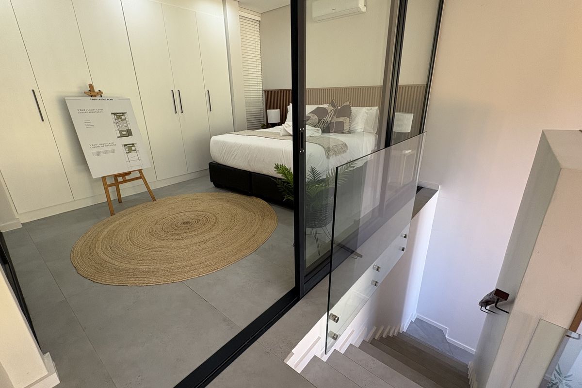 Modern bedroom featuring built-in wardrobes, a stylish slatted timber headboard, and a glass balustrade overlooking the staircase.