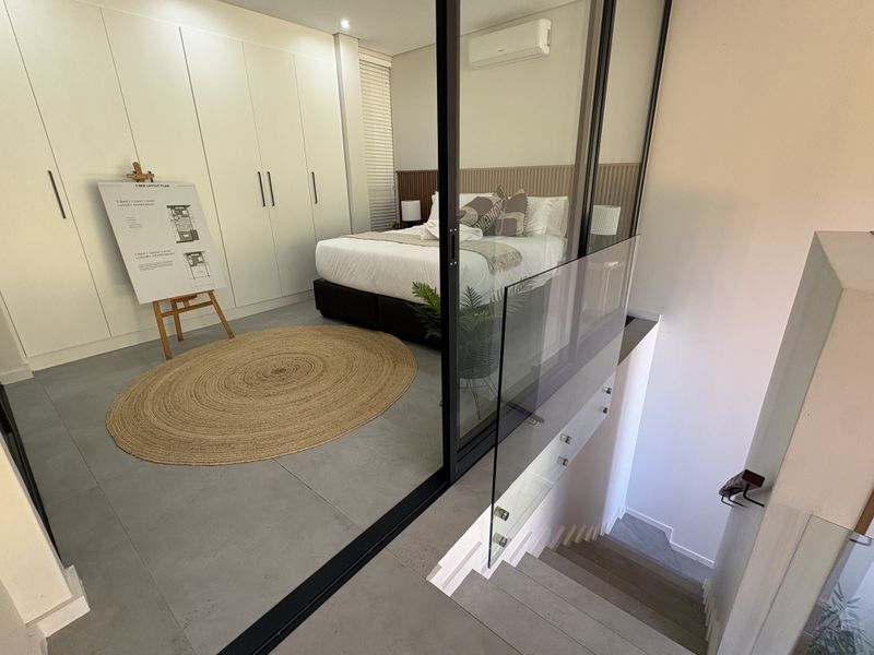 Modern bedroom featuring built-in wardrobes, a stylish slatted timber headboard, and a glass balustrade overlooking the staircase.