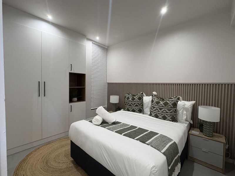 Modern bedroom featuring built-in wardrobes, stylish slatted wood wall paneling, and recessed downlighting, creating a clean and contemporary living space.