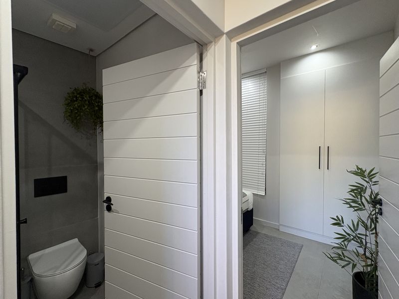 A modern hallway view showing a sleek wall-mounted toilet and a bedroom entrance featuring built-in wardrobes and clean, contemporary finishes.