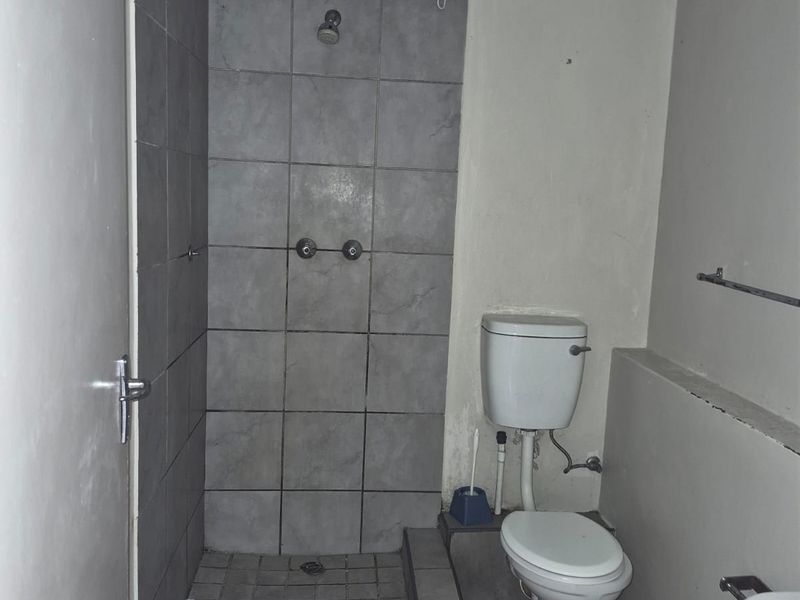 A dated bathroom featuring a tiled shower enclosure, standard toilet, and wash basin, requiring significant cosmetic updates and repairs to finishes.