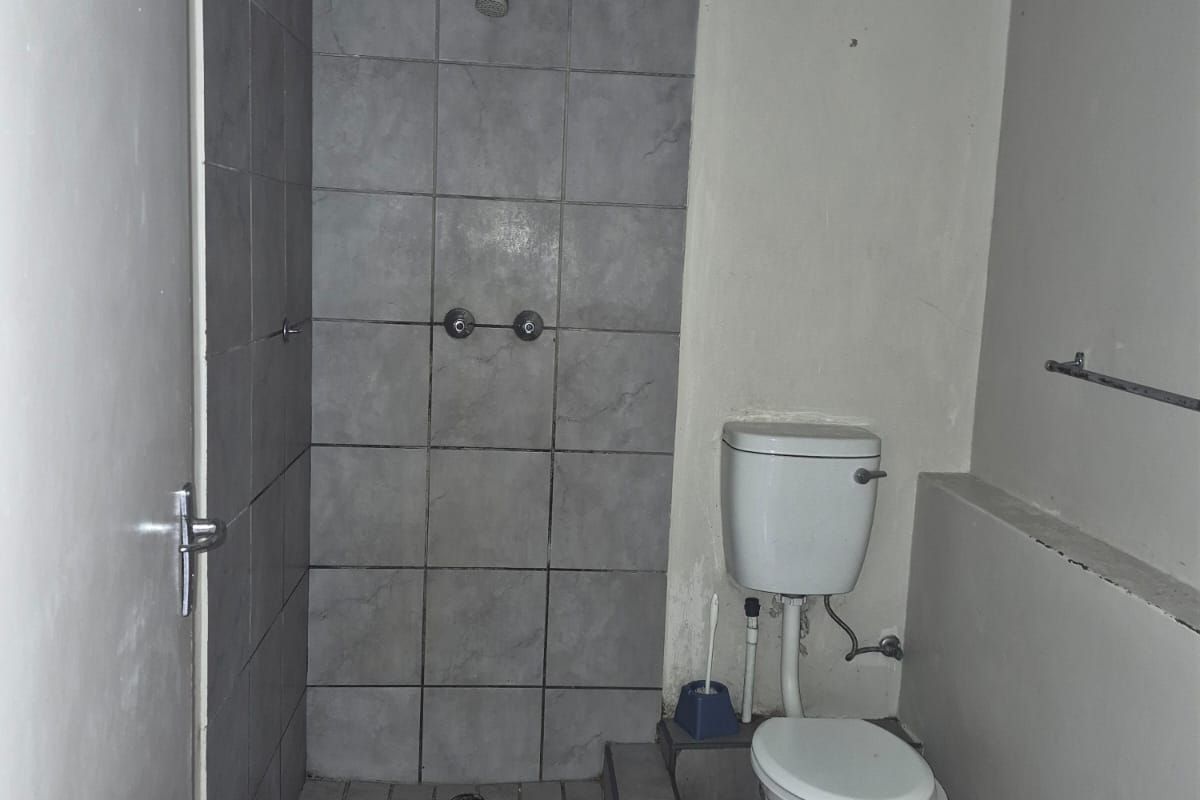 A dated bathroom featuring a tiled shower enclosure, standard toilet, and wash basin, requiring significant cosmetic updates and repairs to finishes.