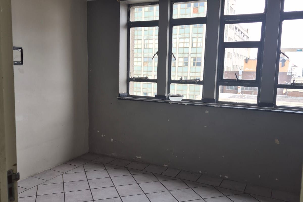 An empty bedroom featuring tiled flooring, a drop ceiling, and large windows. The room requires cosmetic repairs and painting to restore its condition.