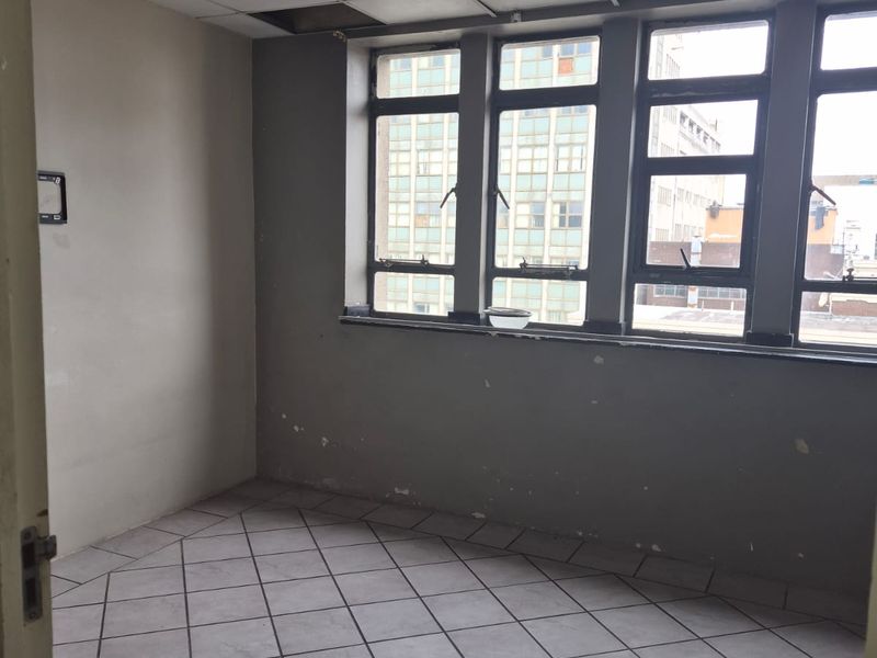 An empty bedroom featuring tiled flooring, a drop ceiling, and large windows. The room requires cosmetic repairs and painting to restore its condition.