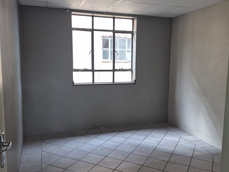 An empty bedroom featuring tiled flooring, a drop ceiling, and a metal-framed window, requiring cosmetic updates to improve its overall condition.