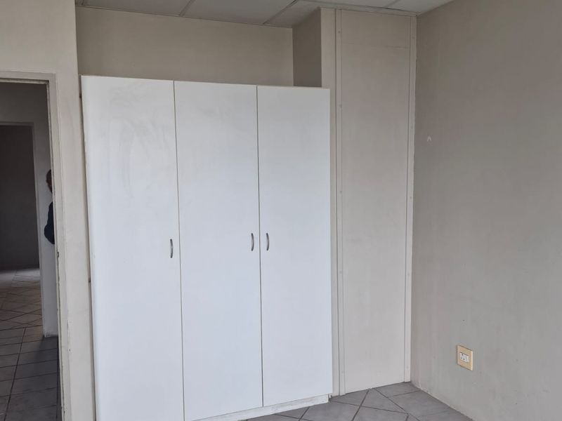 An empty bedroom featuring tiled flooring, a built-in white wardrobe, and a suspended ceiling, offering a blank canvas for renovation.