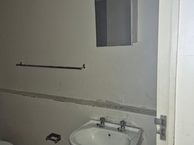 A dated bathroom featuring a pedestal basin, toilet, and medicine cabinet, requiring cosmetic updates and repairs to wall finishes.