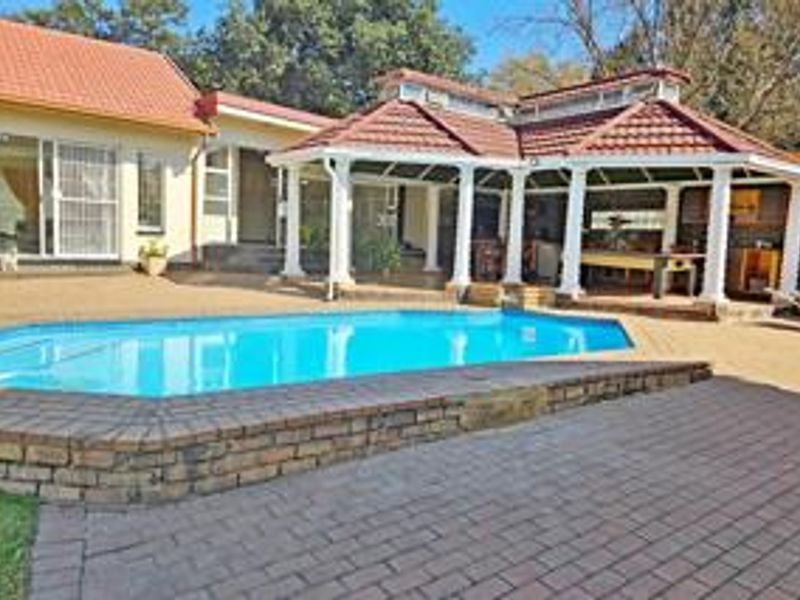 Outdoor entertainment area featuring a swimming pool with a brick-paved surround and a covered patio structure with a tiled roof.