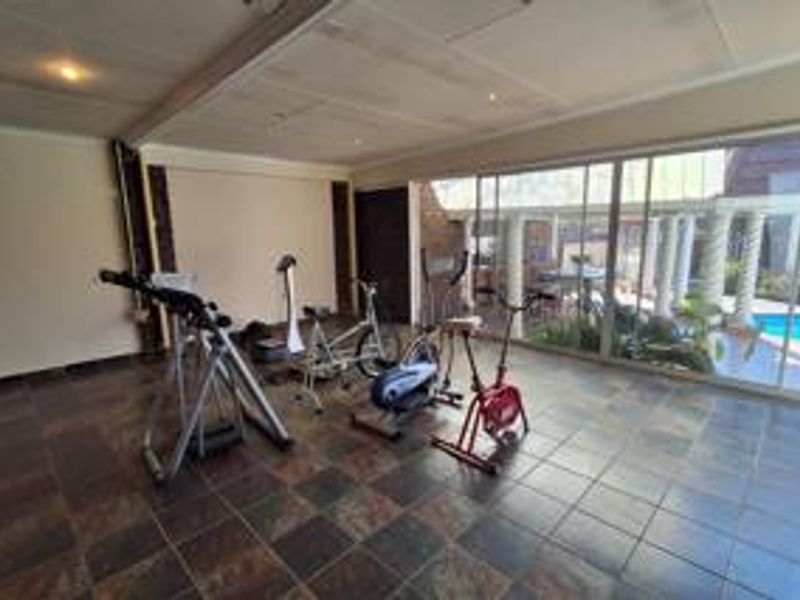 A spacious indoor gym area featuring tiled flooring and large sliding glass doors that provide natural light and views of the pool area.