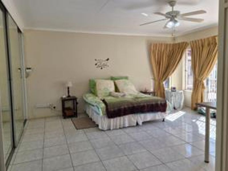 Spacious bedroom featuring tiled flooring, a ceiling fan, and large mirrored sliding wardrobes, offering a functional and well-lit living space.