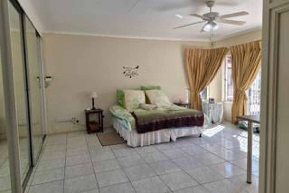 Spacious bedroom featuring tiled flooring, a ceiling fan, and large mirrored sliding wardrobes, offering a functional and well-lit living space.