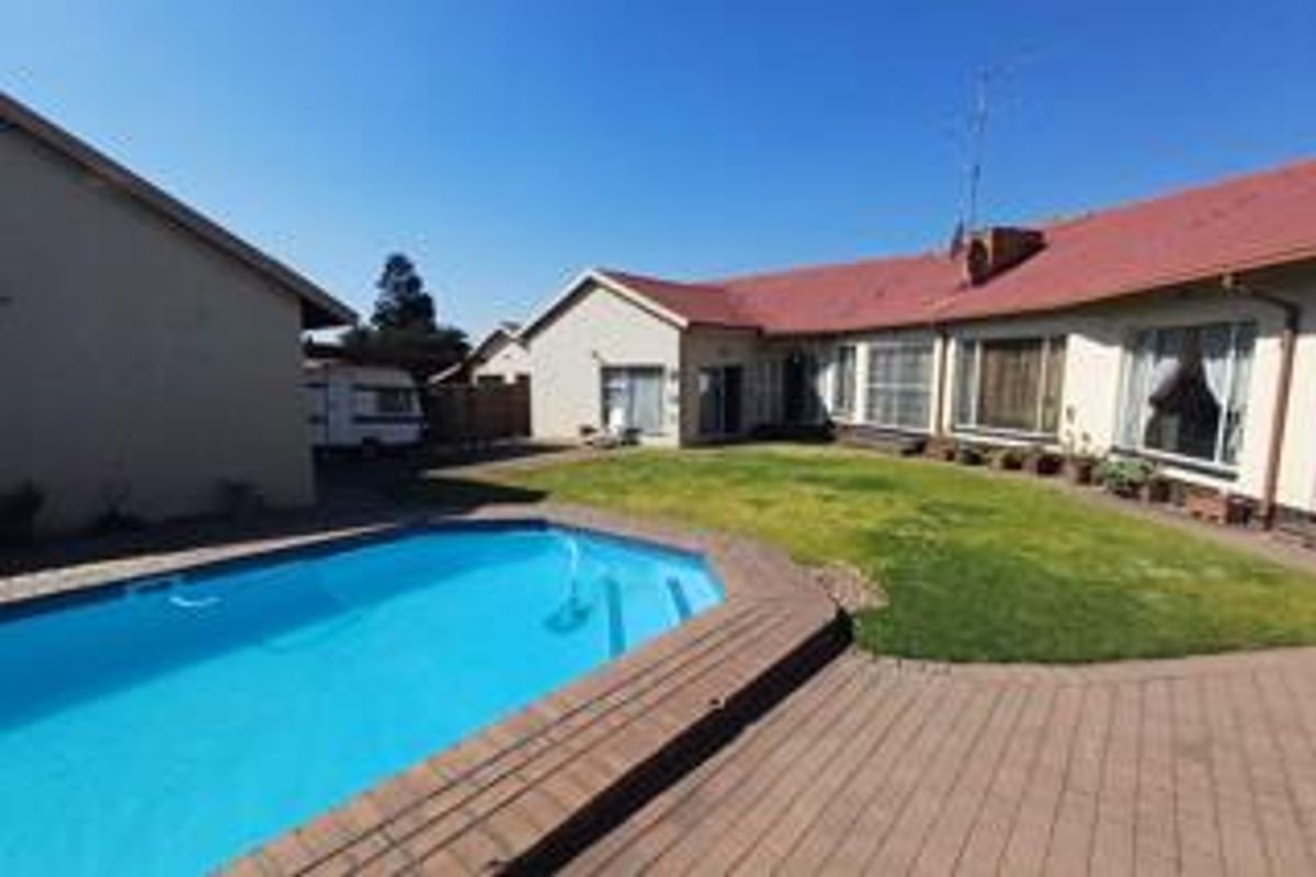 Rear exterior view featuring a swimming pool, paved patio area, and a spacious lawn adjacent to the main house structure.