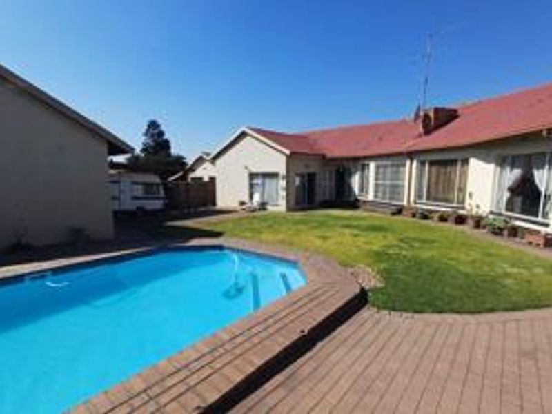Rear exterior view featuring a swimming pool, paved patio area, and a spacious lawn adjacent to the main house structure.