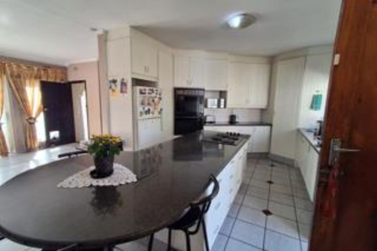 A functional kitchen featuring a large central island with a breakfast bar, built-in oven, hob, and ample cabinetry, finished with tiled flooring.