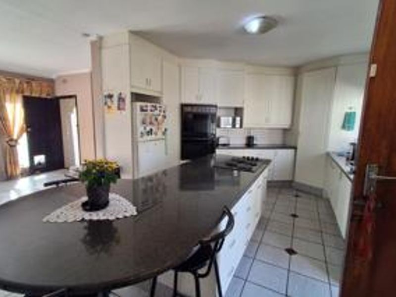 A functional kitchen featuring a large central island with a breakfast bar, built-in oven, hob, and ample cabinetry, finished with tiled flooring.