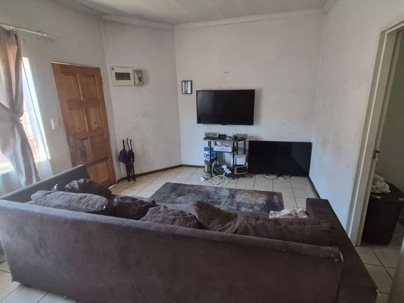 A living room featuring tiled flooring and a timber entrance door, currently showing signs of wear on the walls and finishes.