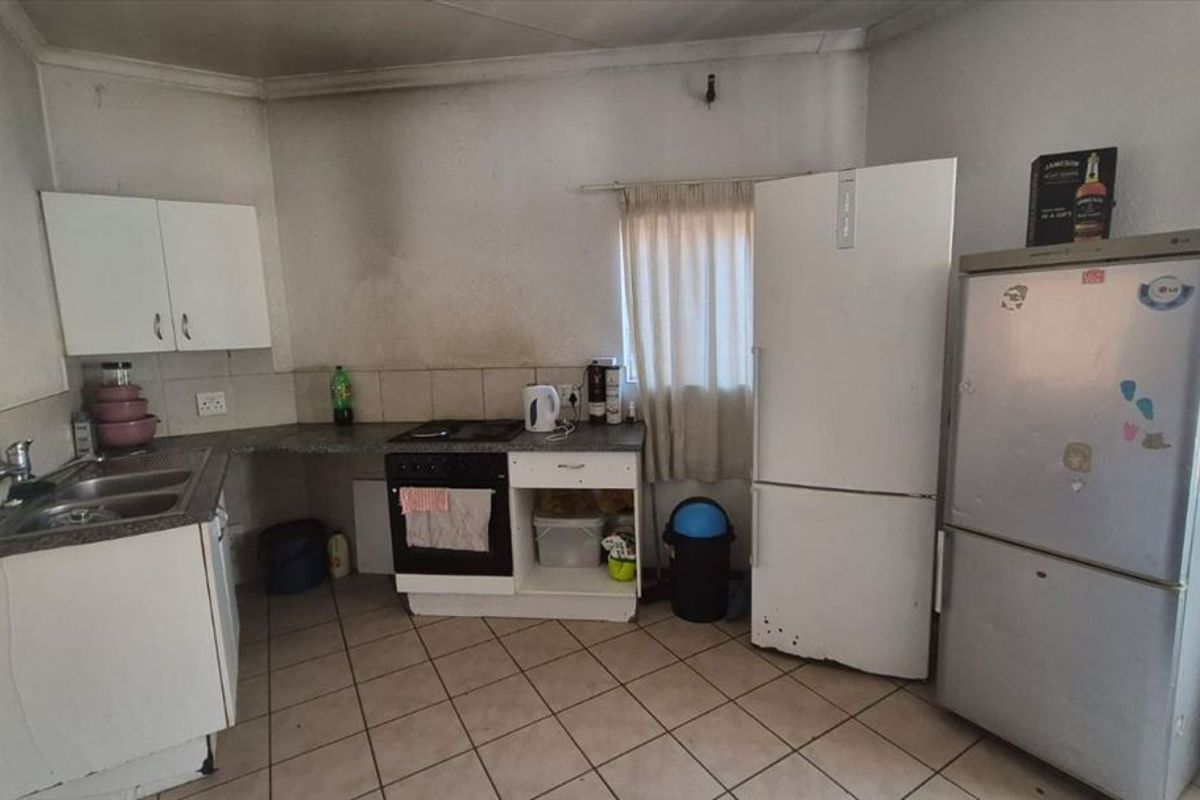 A dated kitchen featuring built-in cabinetry, a stainless steel sink, and a built-in oven, requiring cosmetic updates and wall repairs.