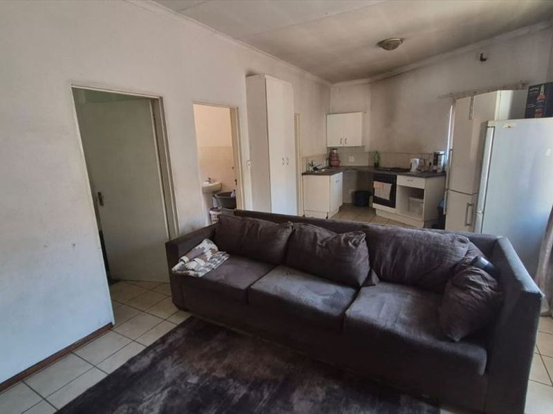 Open plan living and kitchen area featuring tiled floors and built-in cabinetry, requiring significant cosmetic refurbishment and wall repairs.