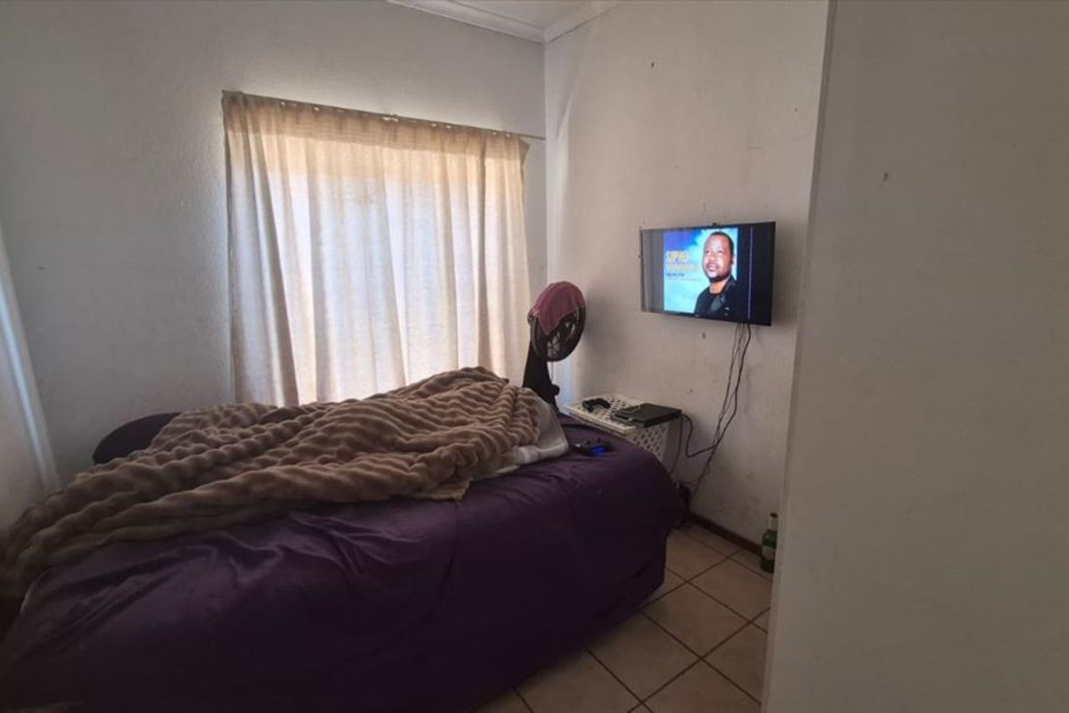 A compact bedroom featuring tiled flooring and a window with a curtain rail, requiring minor cosmetic updates to the wall finishes.