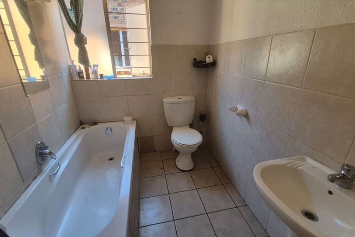 A functional bathroom featuring a bathtub, pedestal sink, and toilet, finished with neutral ceramic wall and floor tiles.
