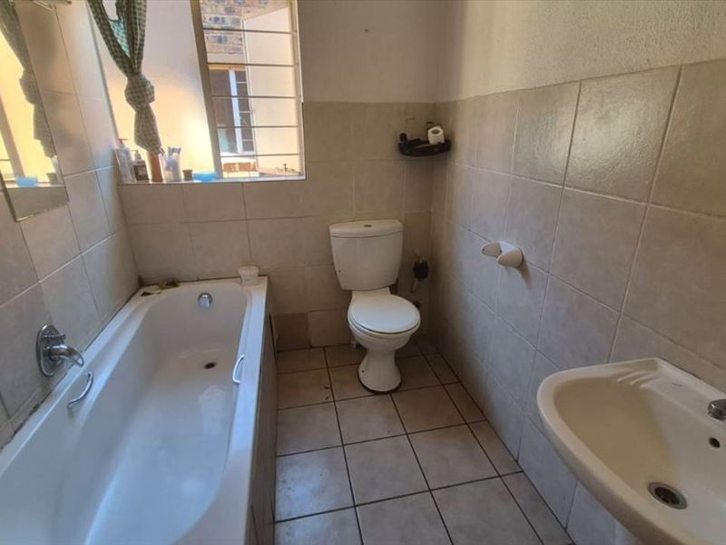 A functional bathroom featuring a bathtub, pedestal sink, and toilet, finished with neutral ceramic wall and floor tiles.