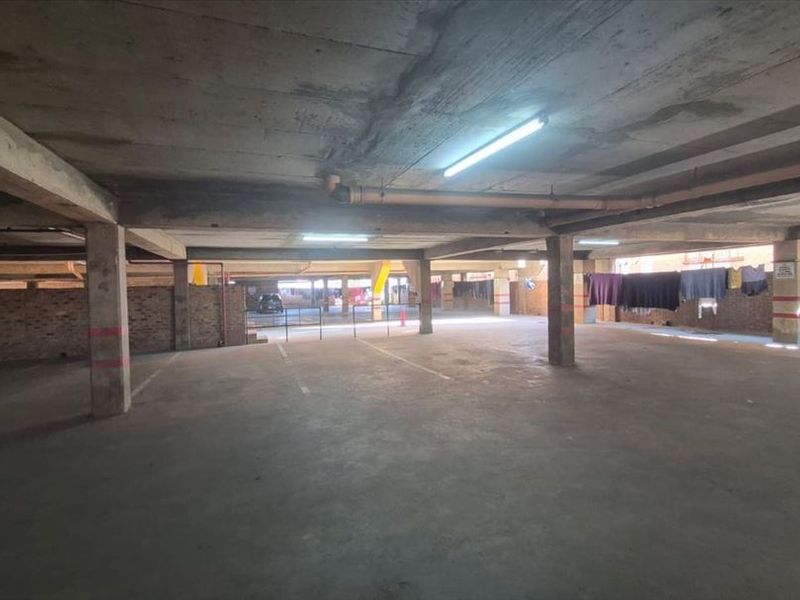 A spacious, open-plan basement parking garage featuring exposed concrete structural elements, brick perimeter walls, and functional overhead lighting.