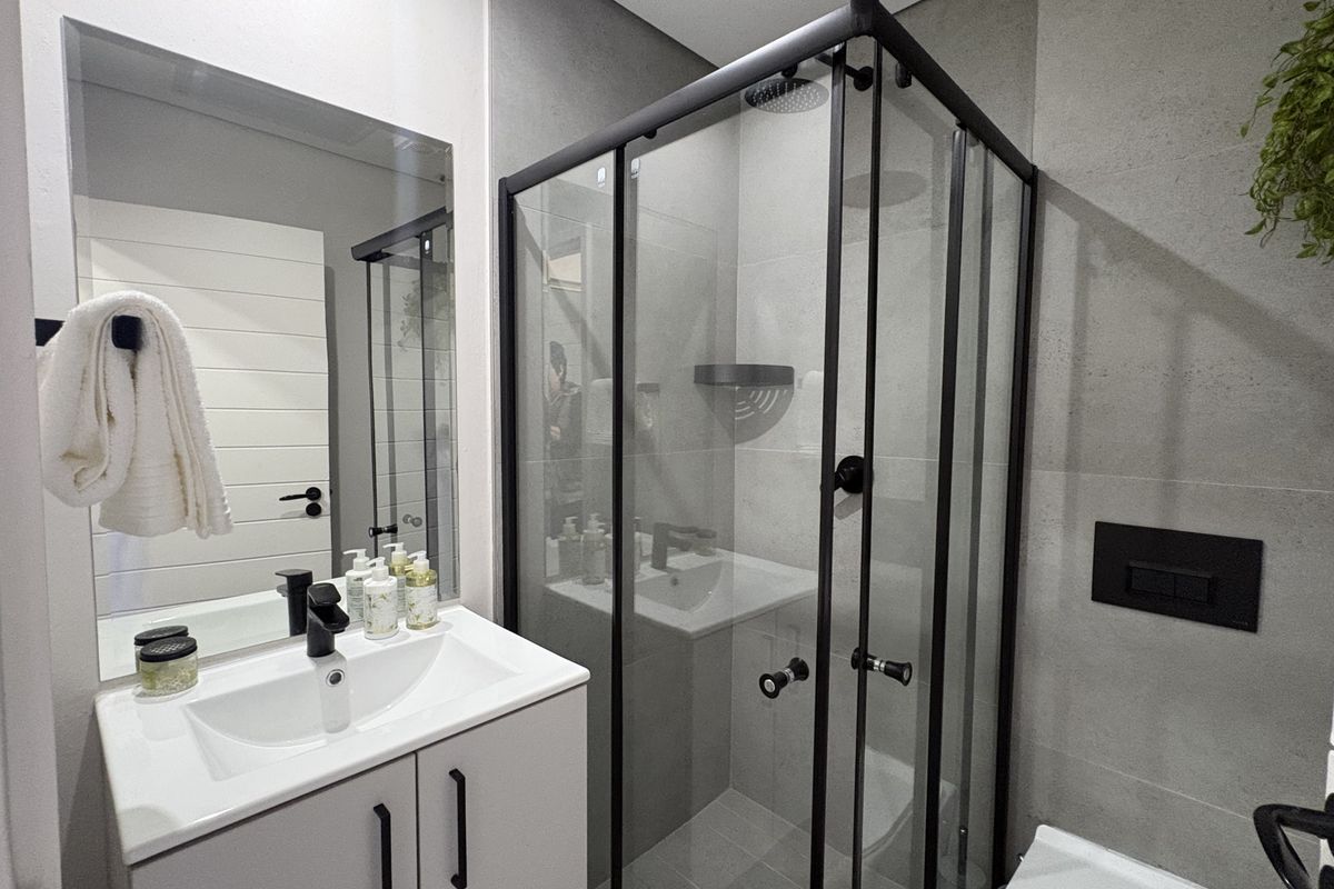 Modern bathroom featuring a sleek vanity with basin, a glass-enclosed shower with black fixtures, and contemporary grey wall tiling.