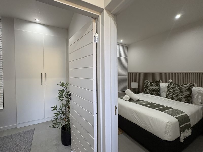 A modern bedroom featuring a built-in wardrobe, slatted timber feature wall, and recessed downlighting, creating a clean and contemporary living space.