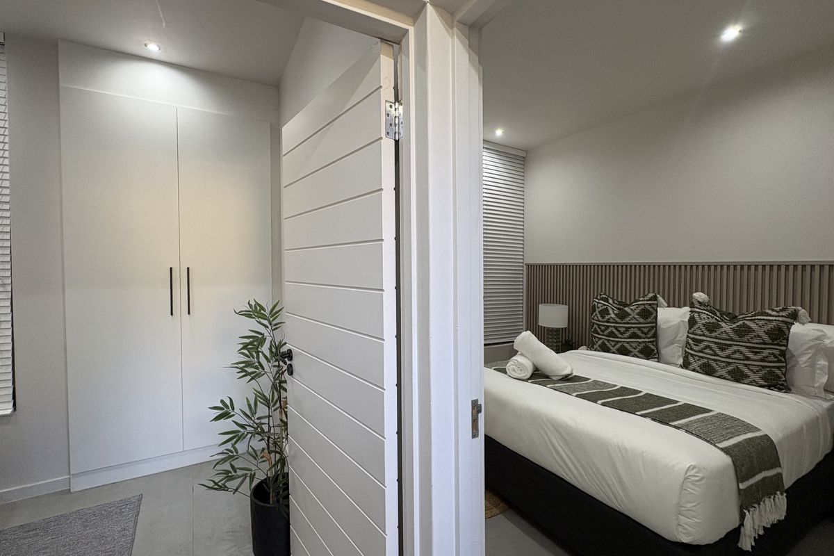 A modern bedroom featuring a built-in wardrobe, slatted timber feature wall, and recessed downlighting, creating a clean and contemporary living space.