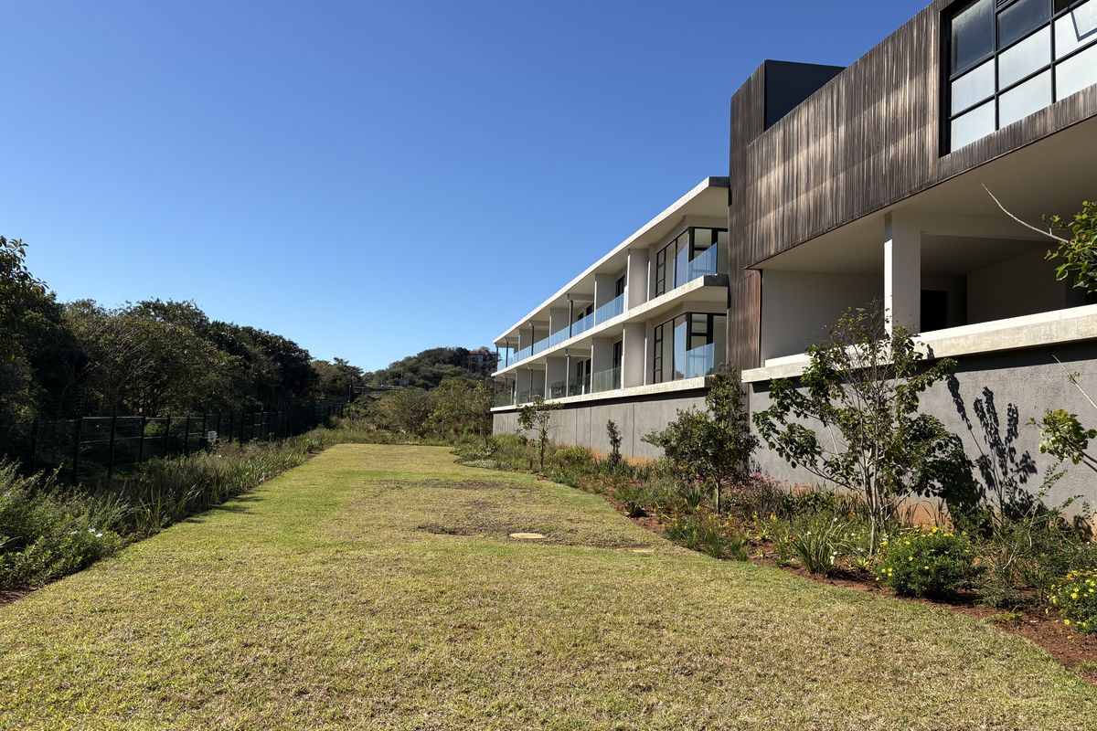A view of the rear elevation of a modern apartment building featuring timber cladding, glass-fronted balconies, and a well-maintained landscaped garden area.