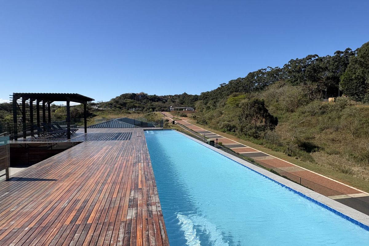 An elevated infinity pool area featuring extensive timber decking, a pergola structure, and glass balustrades overlooking a scenic landscape.
