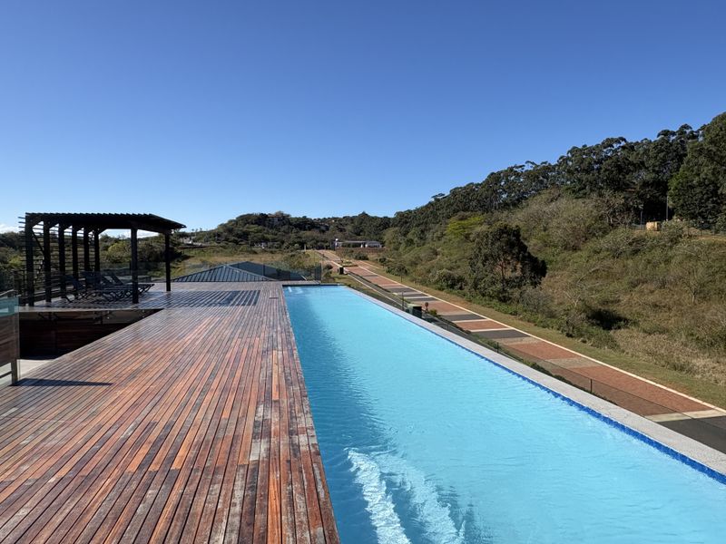 An elevated infinity pool area featuring extensive timber decking, a pergola structure, and glass balustrades overlooking a scenic landscape.