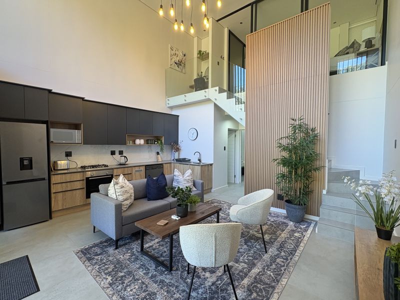 Modern open-plan living area featuring a sleek kitchen with built-in appliances, timber slat feature wall, and a staircase with glass balustrade.