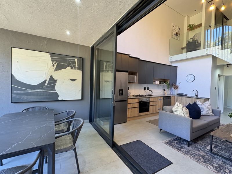 Modern open-plan living area featuring a sleek kitchen with built-in appliances, double-height ceilings, and seamless indoor-outdoor flow through large sliding glass doors.