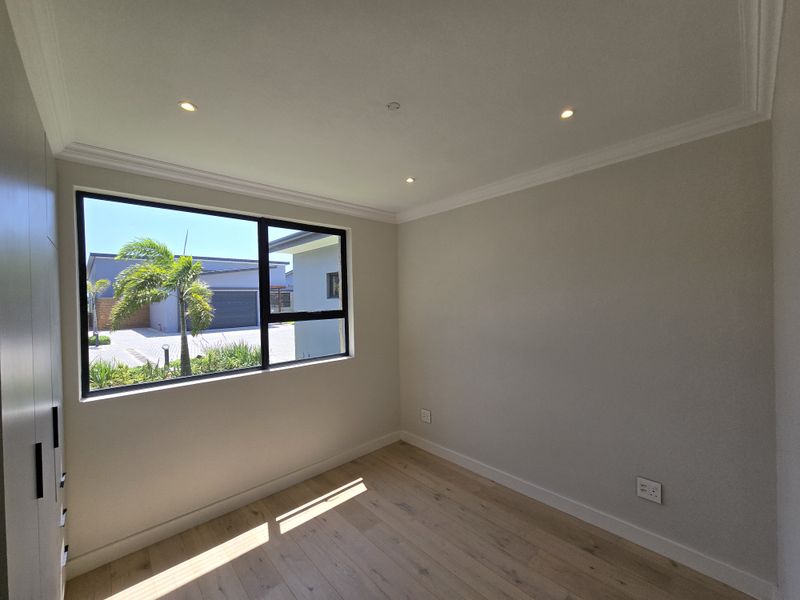 A bright, empty bedroom featuring modern laminate flooring, built-in cupboards, recessed downlights, and a large window with views of the exterior.