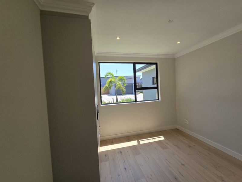 A bright, empty bedroom featuring modern timber flooring, built-in cupboards, recessed downlights, and elegant cornicing.