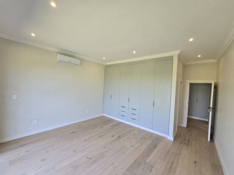 Spacious bedroom featuring light timber flooring, extensive built-in cabinetry, recessed lighting, and a wall-mounted air conditioning unit.