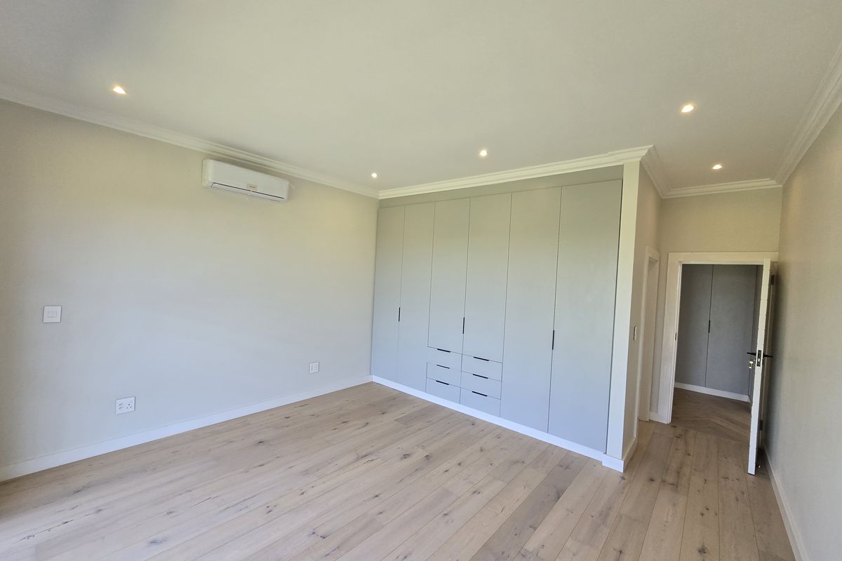 Spacious bedroom featuring light timber flooring, extensive built-in cabinetry, recessed lighting, and a wall-mounted air conditioning unit.